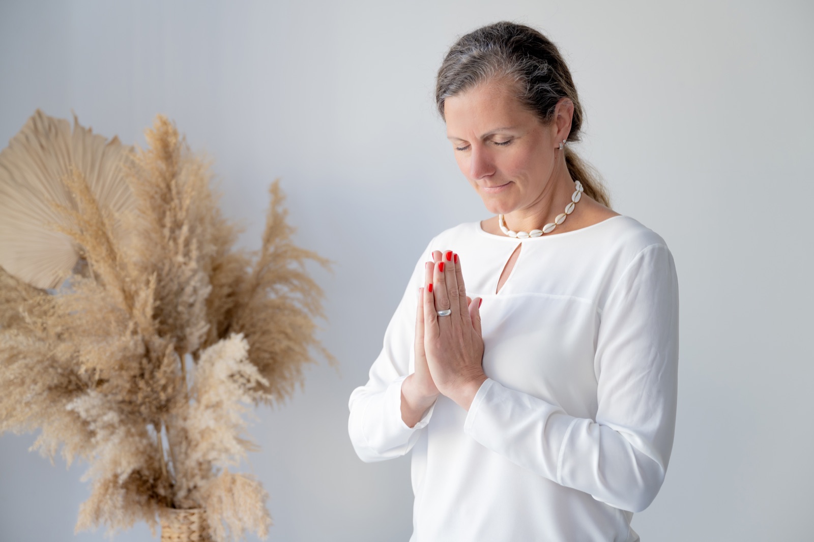 Nicole Melior in meditativer Haltung mit gefalteten Händen vor getrockneten Pampasgräsern